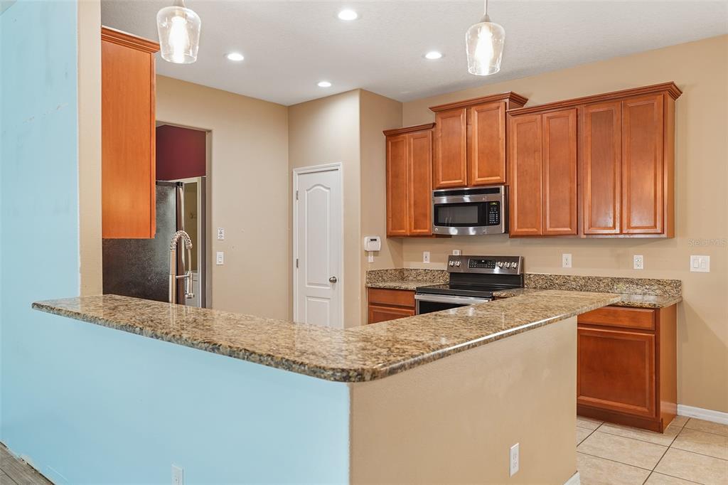 A kitchen features wood cabinets, granite countertops, a breakfast bar, and stainless steel appliances — 3205 BAYFLOWER AVE, ST CLOUD, FL