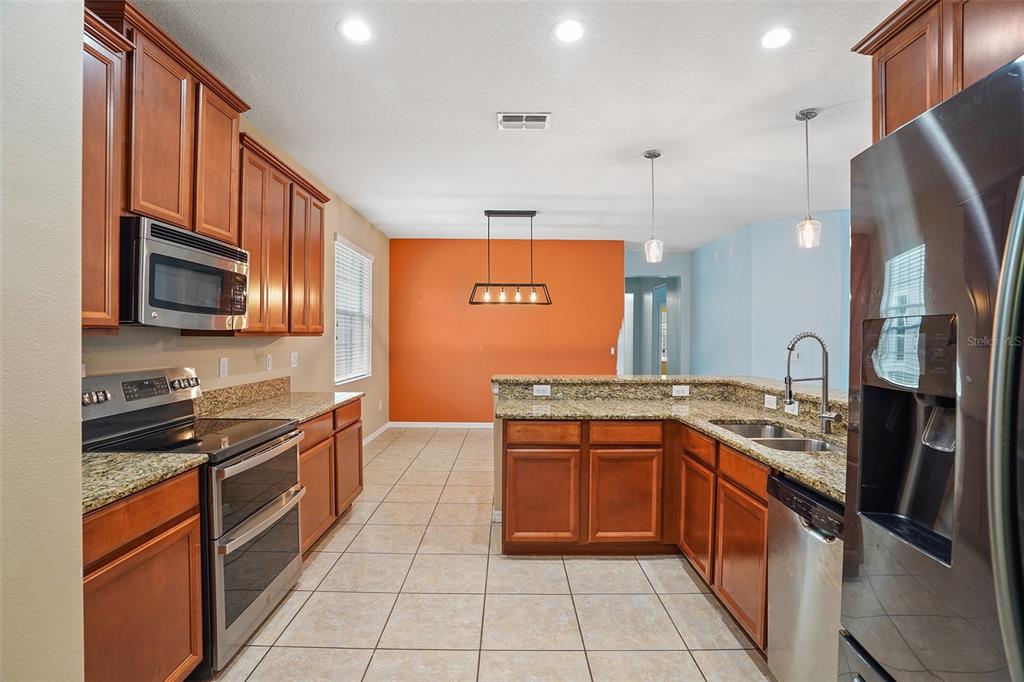 A kitchen with wood cabinets, granite countertops, stainless steel appliances, and an orange accent wall — 3205 BAYFLOWER AVE, ST CLOUD, FL