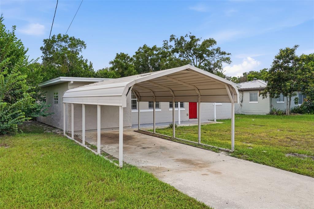 A beige house with a red front door features a metal carport over a concrete driveway — 218 5TH JPV STREET, WINTER HAVEN, FL