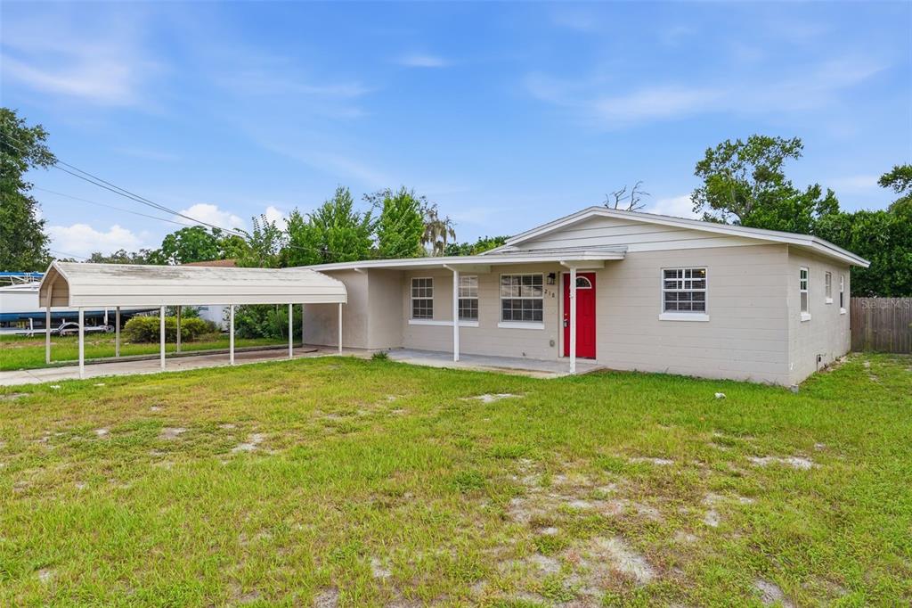A single-story house with a beige exterior, a red front door, and an attached metal carport — 218 5TH JPV STREET, WINTER HAVEN, FL