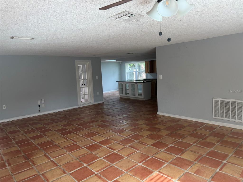 A spacious room with terracotta tile flooring leads to a kitchen with a breakfast bar — 9830 MARK TWAIN LANE, PORT RICHEY, FL