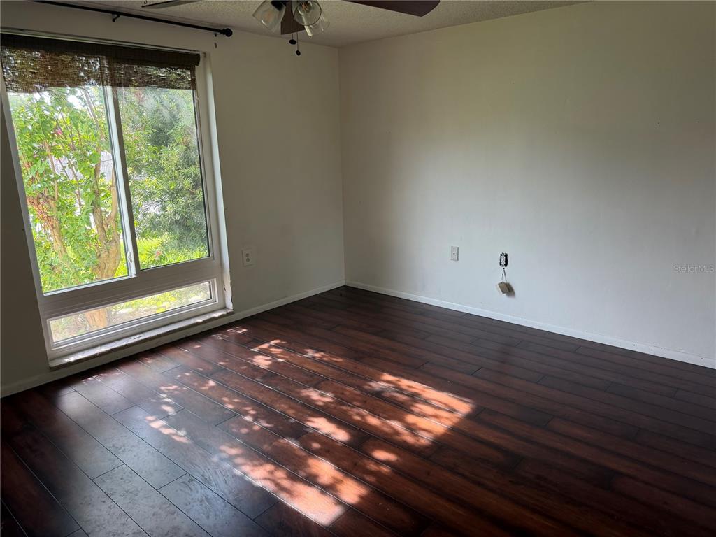 An empty bedroom features dark wood-look flooring, white walls, and a large window — 9830 MARK TWAIN LANE, PORT RICHEY, FL