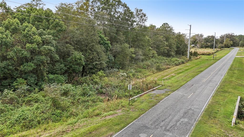 An elevated view shows a paved road running alongside a dense, wooded area and grass — 0 W EDWARDS ROAD, STARKE, FL