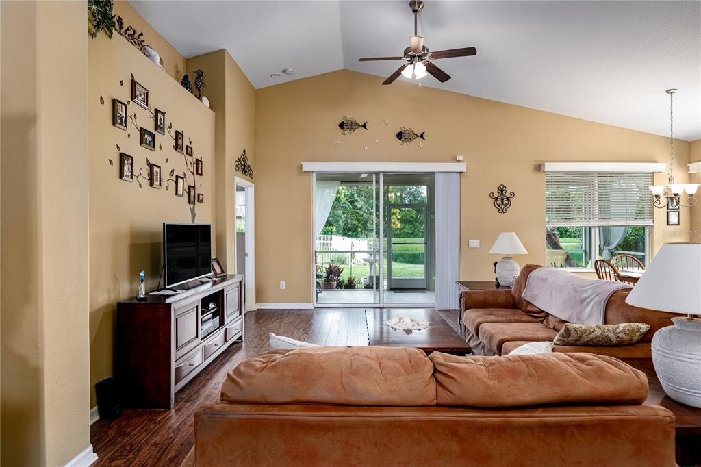 A living room with tan walls, a vaulted ceiling, brown sofas, and a sliding glass door — 3628 101ST AVENUE E, PARRISH, FL