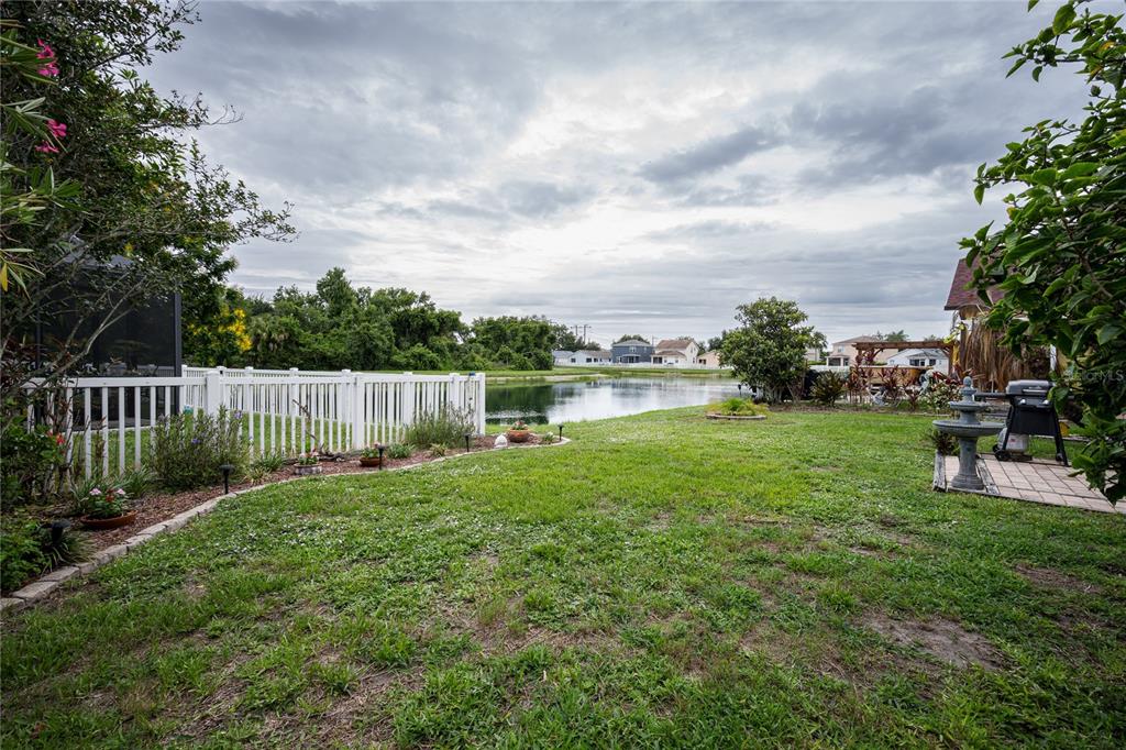 A grassy backyard features a white fence, a small pond, and a patio with a grill — 3628 101ST AVENUE E, PARRISH, FL