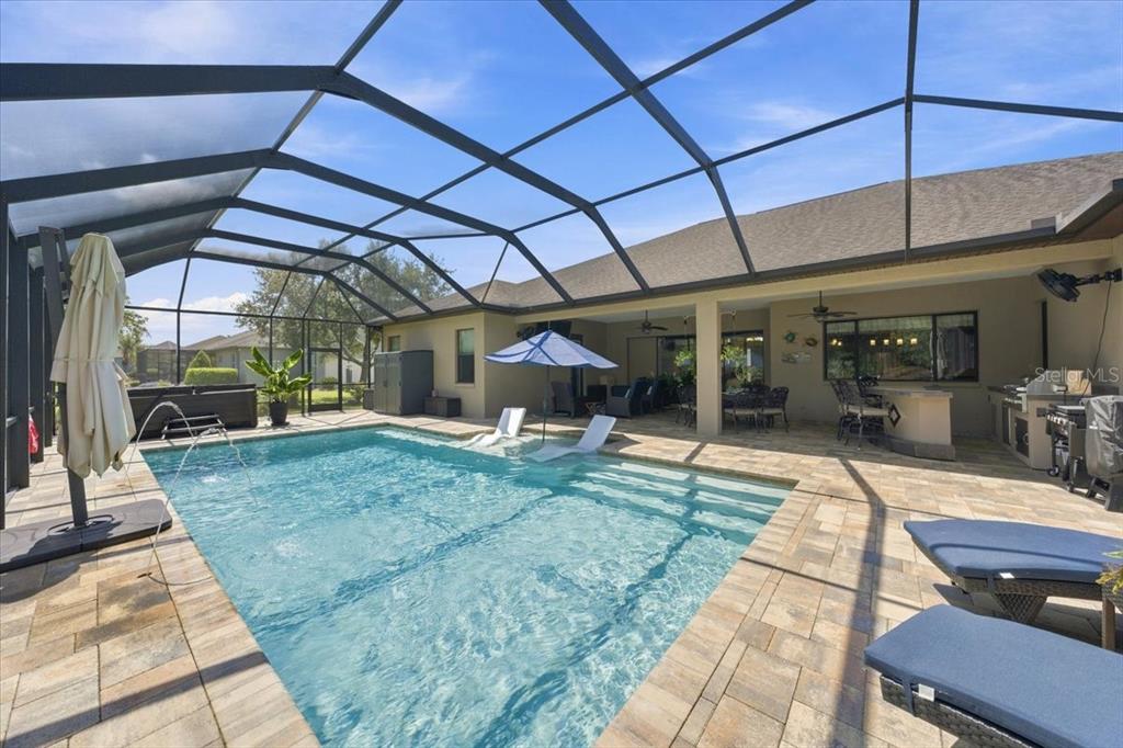 A screened-in patio features a swimming pool with a tanning ledge and outdoor kitchen — 408 HAWK TALON DRIVE, LITHIA, FL