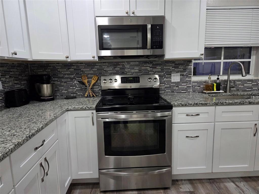 A kitchen features white cabinets, granite countertops, a stainless steel stove, and a tiled backsplash — 8024 CANDLEWOODE DRIVE, LARGO, FL