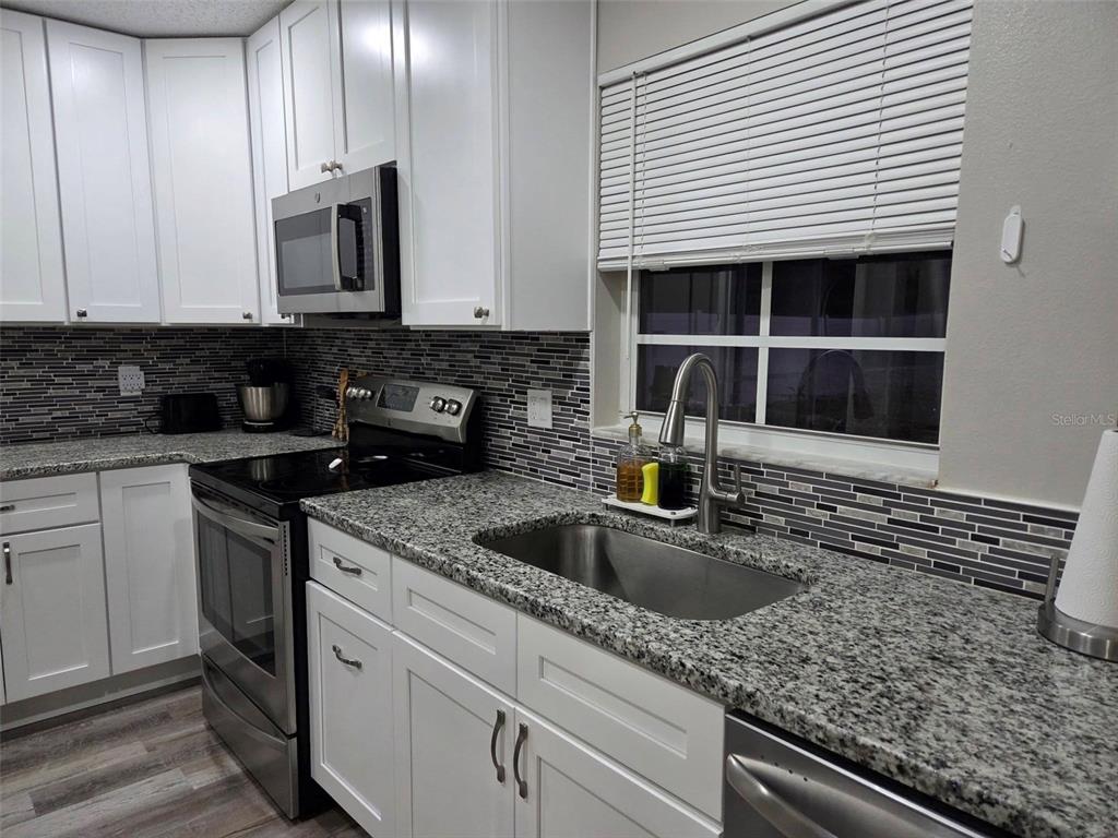 A kitchen features white cabinets, granite countertops, a stainless steel stove, and a tiled backsplash — 8024 CANDLEWOODE DRIVE, LARGO, FL