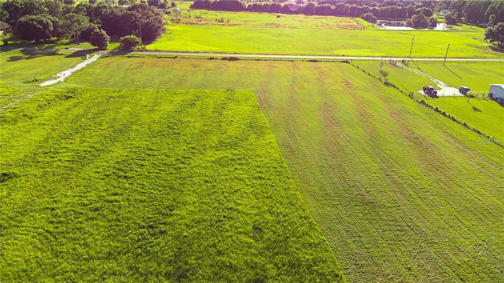 An aerial view shows a large, open grassy field with a road and nearby trees — 34400 SR-62, PARRISH, FL