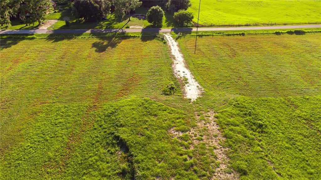 An aerial view shows a grassy field with a dirt path leading to a road — 34400 SR-62, PARRISH, FL