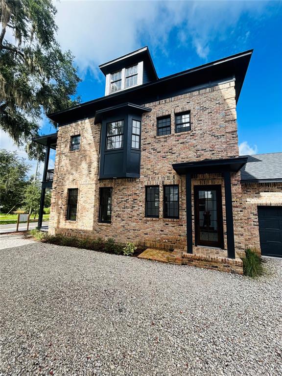 A three-story brick house with black trim and a gravel driveway under a blue sky — 294 NW 12TH AVENUE, GAINESVILLE, FL