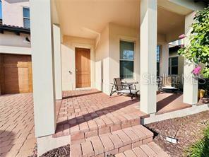 A covered front porch with brick pavers, a wooden door, and a metal patio chair — 15155 CANOE PLACE, WINTER GARDEN, FL