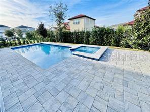 A backyard features a rectangular swimming pool and attached spa surrounded by light-colored stone pavers — 15155 CANOE PLACE, WINTER GARDEN, FL