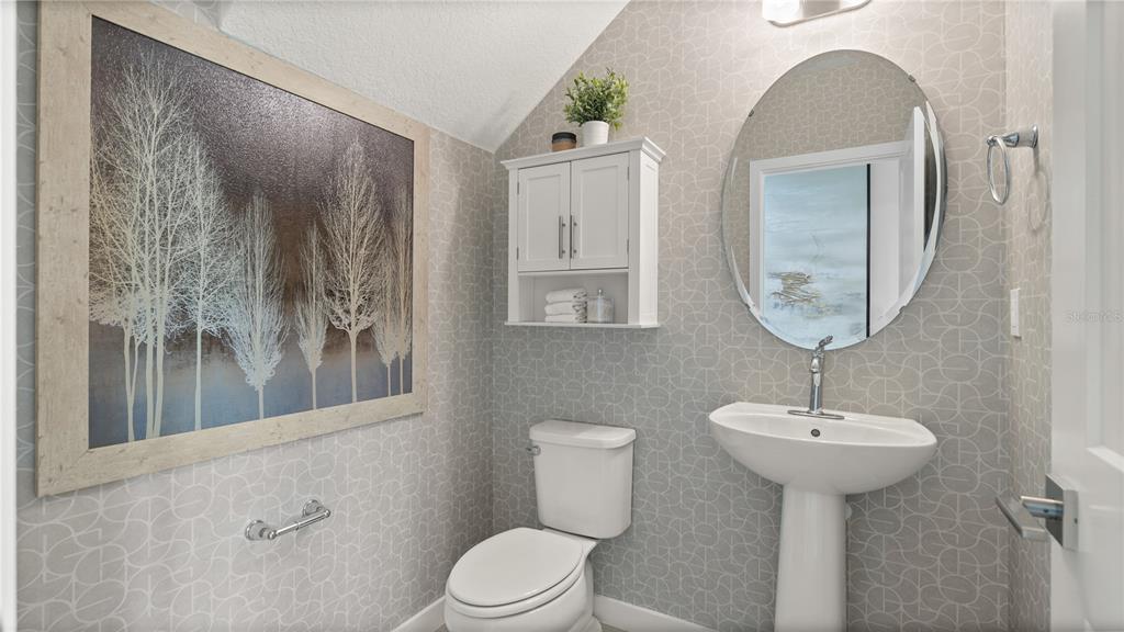 A small bathroom features a pedestal sink, a toilet, a wall cabinet, and patterned wallpaper — 1964 DIAMOND HEAD CIRCLE, LAKE HAMILTON, FL