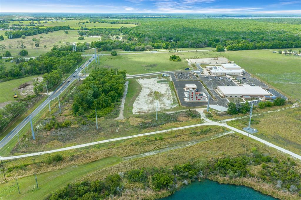 An aerial view shows a commercial building complex surrounded by undeveloped land and a pond — 178 N US 301, SUMTERVILLE, FL