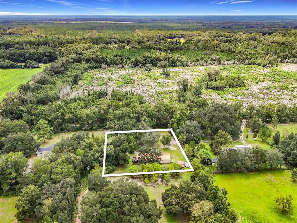 An aerial view shows a house situated on a wooded lot outlined in white — 13906 SW 132ND PLACE, ARCHER, FL
