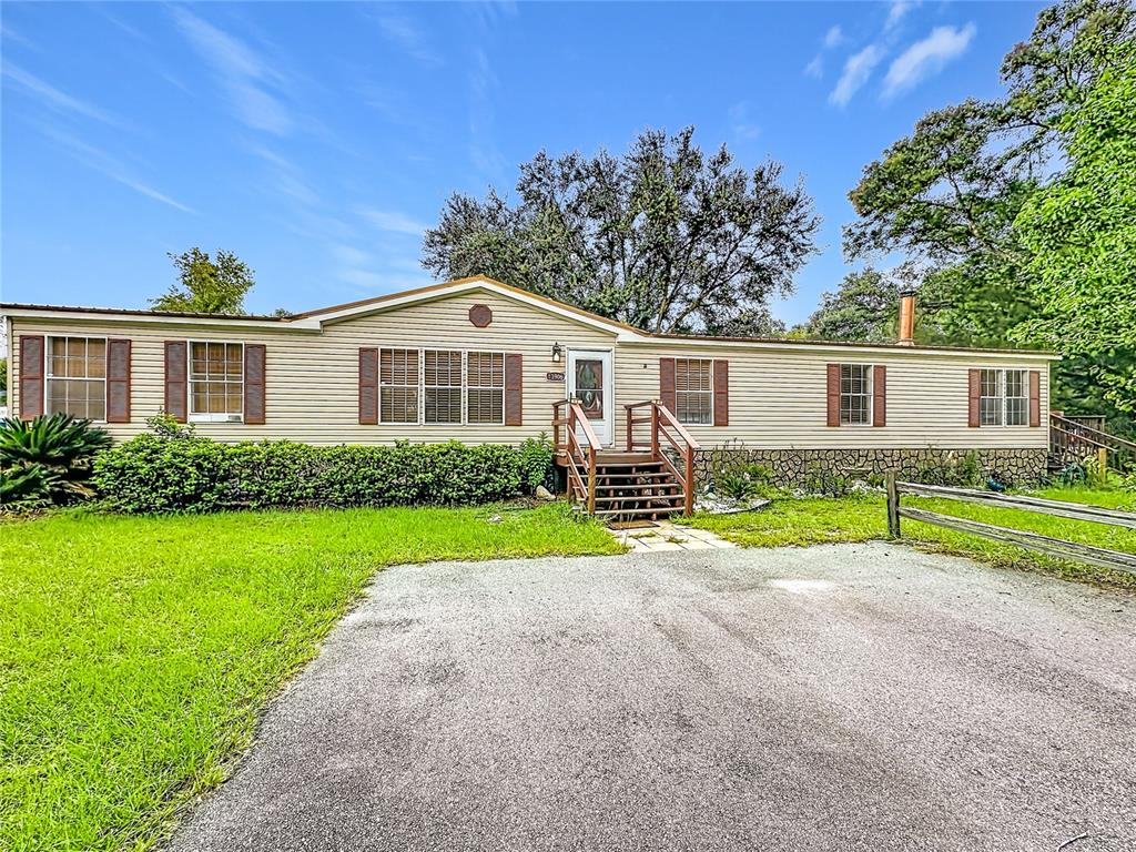 A single-story manufactured home with beige siding, brown shutters, and a wooden front porch — 13906 SW 132ND PLACE, ARCHER, FL