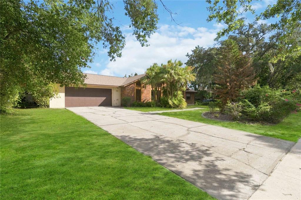 A single-story brick house with a large concrete driveway and a two-car garage — 7813 SARANAC COURT, ORLANDO, FL