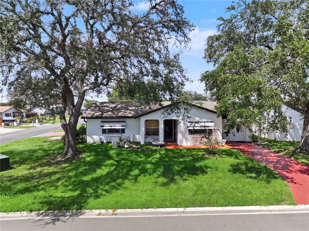 A single-story white brick house with a red driveway and large trees in the yard — 99 TOLUCA DRIVE, KISSIMMEE, FL