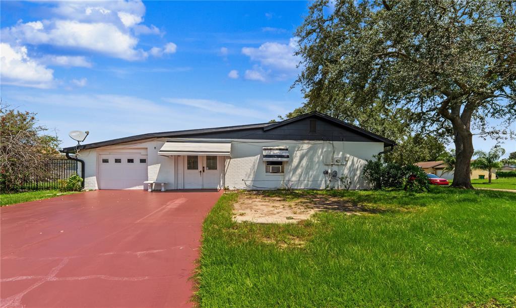 A single-story white brick house features a red driveway, a garage, and a large tree — 99 TOLUCA DRIVE, KISSIMMEE, FL