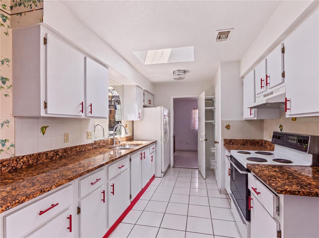A kitchen features white cabinets with red handles, brown patterned countertops, and white tile flooring — 99 TOLUCA DRIVE, KISSIMMEE, FL
