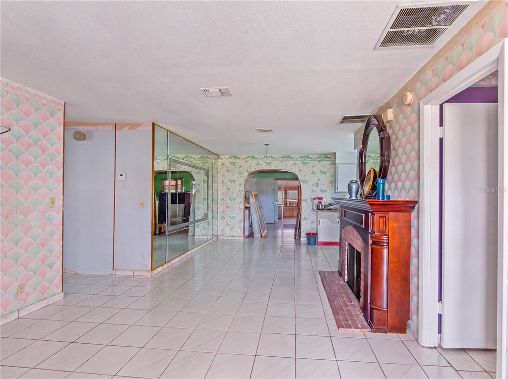 A living room features tiled floors, patterned wallpaper, a mirrored wall, and a wooden fireplace — 99 TOLUCA DRIVE, KISSIMMEE, FL