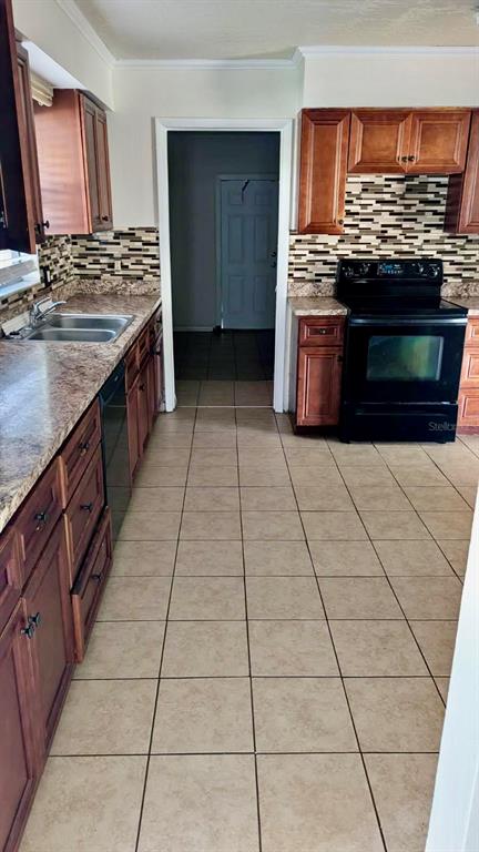 A kitchen features wood cabinets, a black stove, a tiled backsplash, and light-colored floor tiles — 1077 BASQUE DRIVE, ROCKLEDGE, FL