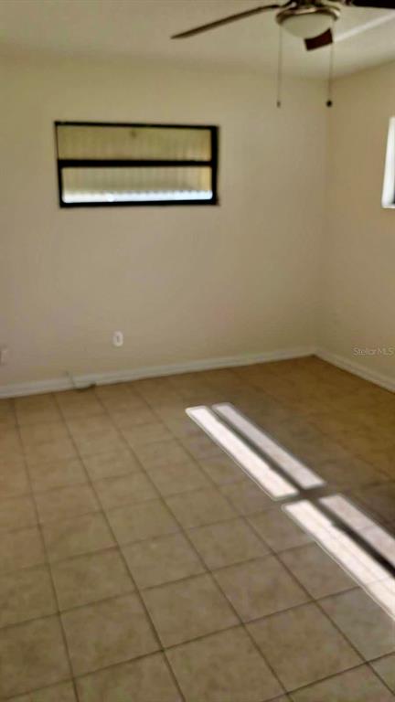 An empty room features beige tiled flooring, light-colored walls, and a ceiling fan — 1077 BASQUE DRIVE, ROCKLEDGE, FL