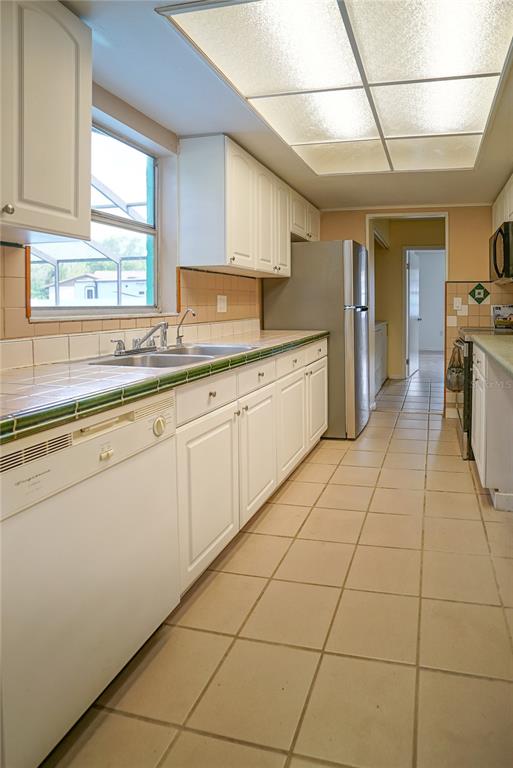 A galley kitchen features white cabinets, tiled countertops, a stainless steel refrigerator, and tile flooring — 3320 LAS BRISAS DRIVE, RIVERVIEW, FL