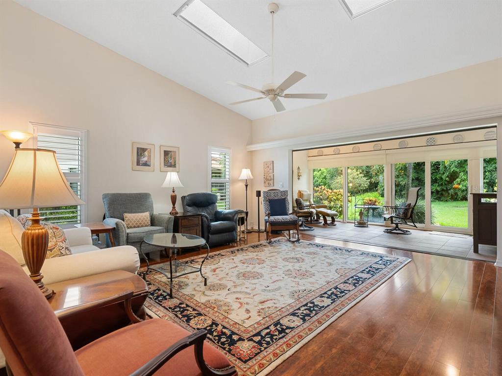 A living room with hardwood floors, a large area rug, and sliding doors to a patio — 4004 WILSHIRE CIRCLE E UNIT 89, SARASOTA, FL