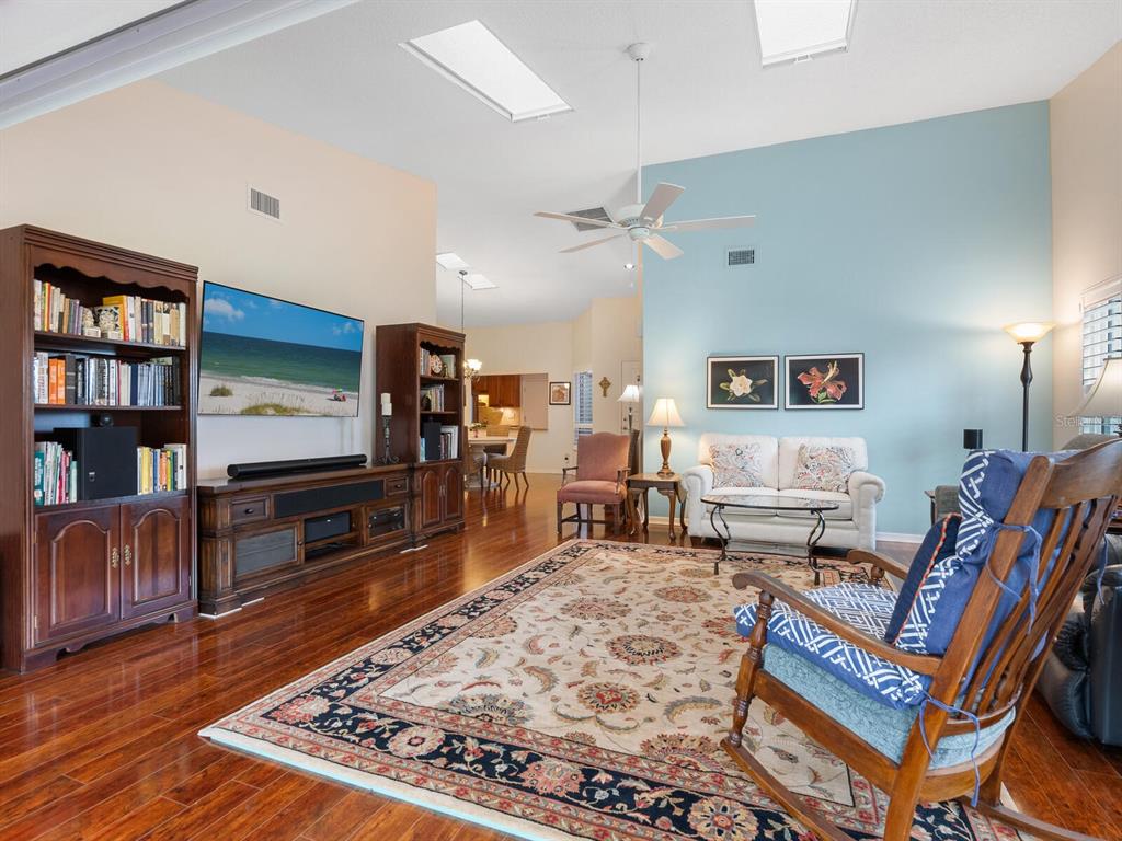 A living room with hardwood floors, a large area rug, and a light blue wall — 4004 WILSHIRE CIRCLE E UNIT 89, SARASOTA, FL