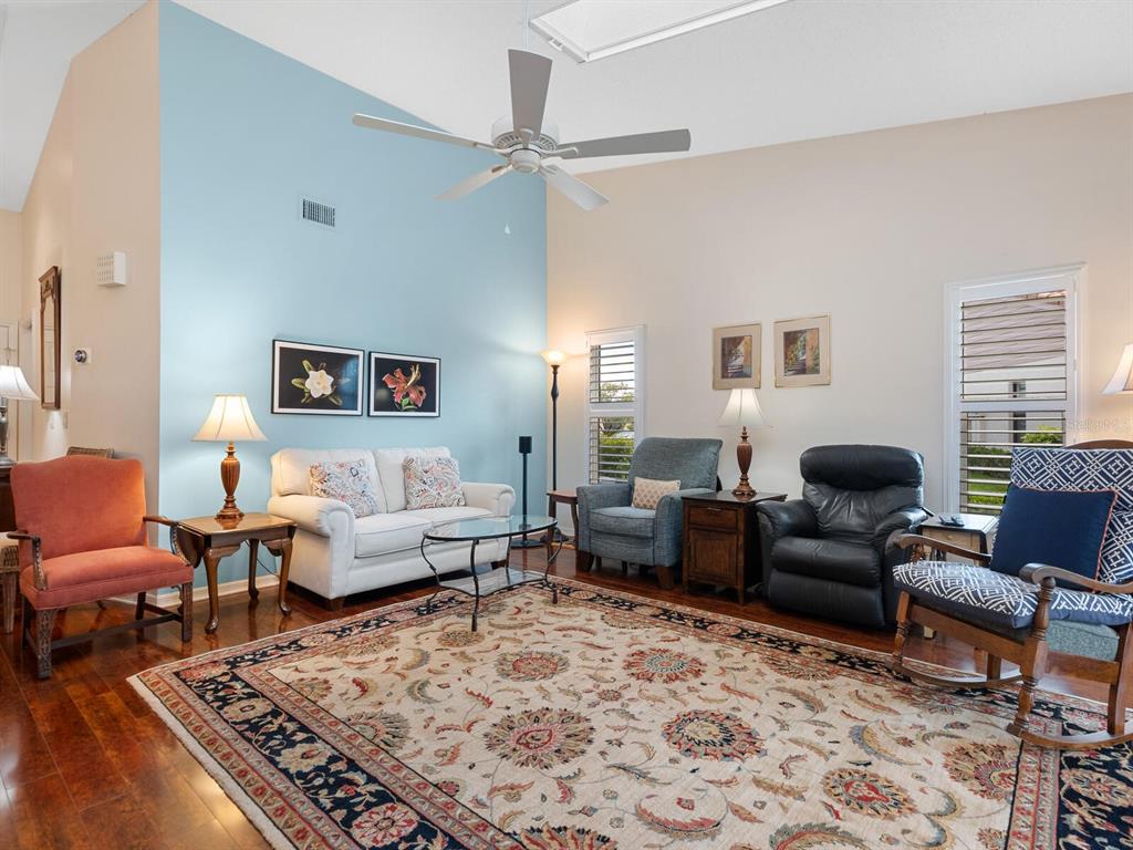 A living room features a vaulted ceiling, a blue accent wall, and a patterned area rug — 4004 WILSHIRE CIRCLE E UNIT 89, SARASOTA, FL