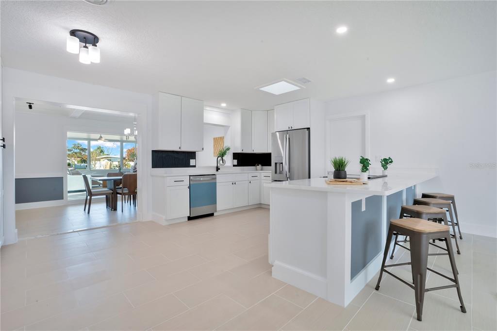 A modern kitchen features white cabinetry, a central island with bar stools, and tiled flooring — 2801 GULFSTREAM ROAD, ORLANDO, FL