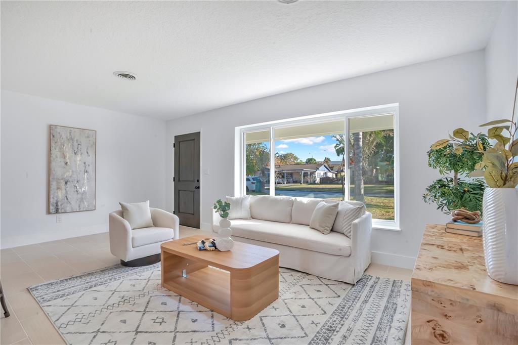 A bright living room features a white sofa, an armchair, a coffee table, and large windows — 2801 GULFSTREAM ROAD, ORLANDO, FL