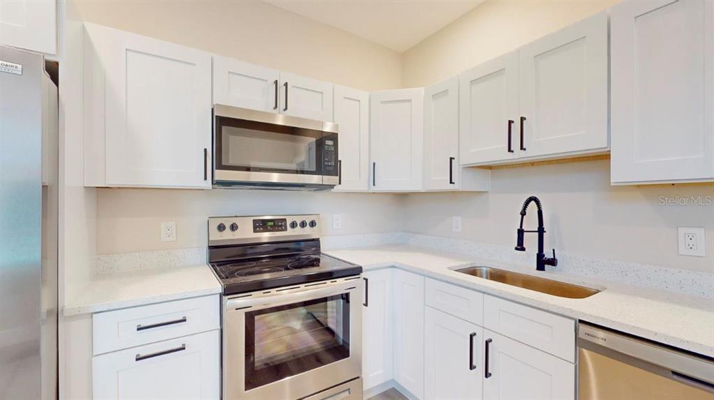 A kitchen features white cabinets, stainless steel appliances, a black faucet, and light countertops — 5113 12TH AVENUE N, ST PETERSBURG, FL