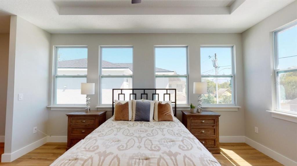 A bedroom features a bed centered against four windows with light walls and wood floors — 5113 12TH AVENUE N, ST PETERSBURG, FL
