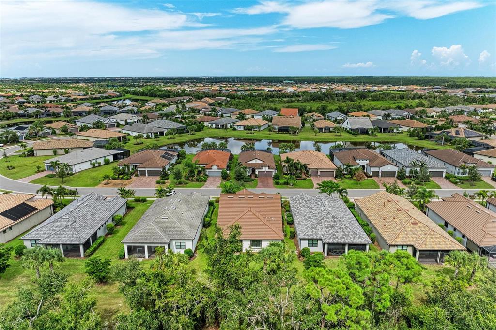 An aerial view shows a suburban neighborhood with houses surrounding a central pond — 7572 VIOLA LOOP, BRADENTON, FL
