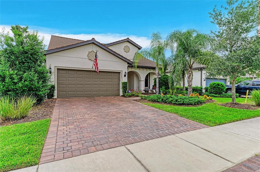 A single-story house with a brown garage door, brick paver driveway, and palm trees — 7572 VIOLA LOOP, BRADENTON, FL