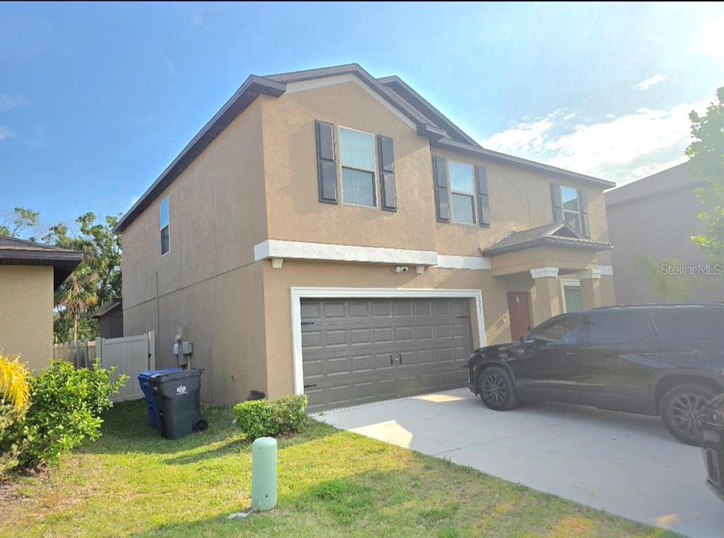 A two-story tan stucco house with a dark brown garage door and a driveway — 1561 FLOWER DUST DRIVE, RUSKIN, FL