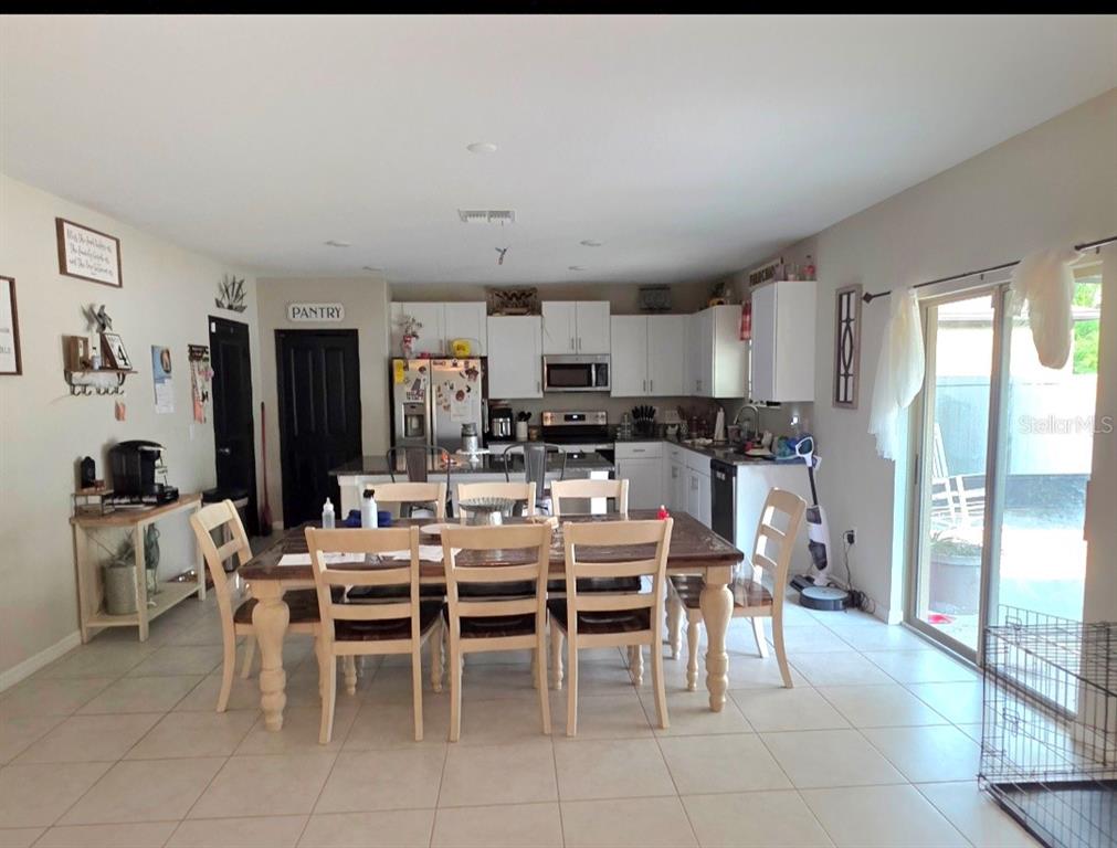 A kitchen and dining area with white cabinets, a wooden table, and tile flooring — 1561 FLOWER DUST DRIVE, RUSKIN, FL