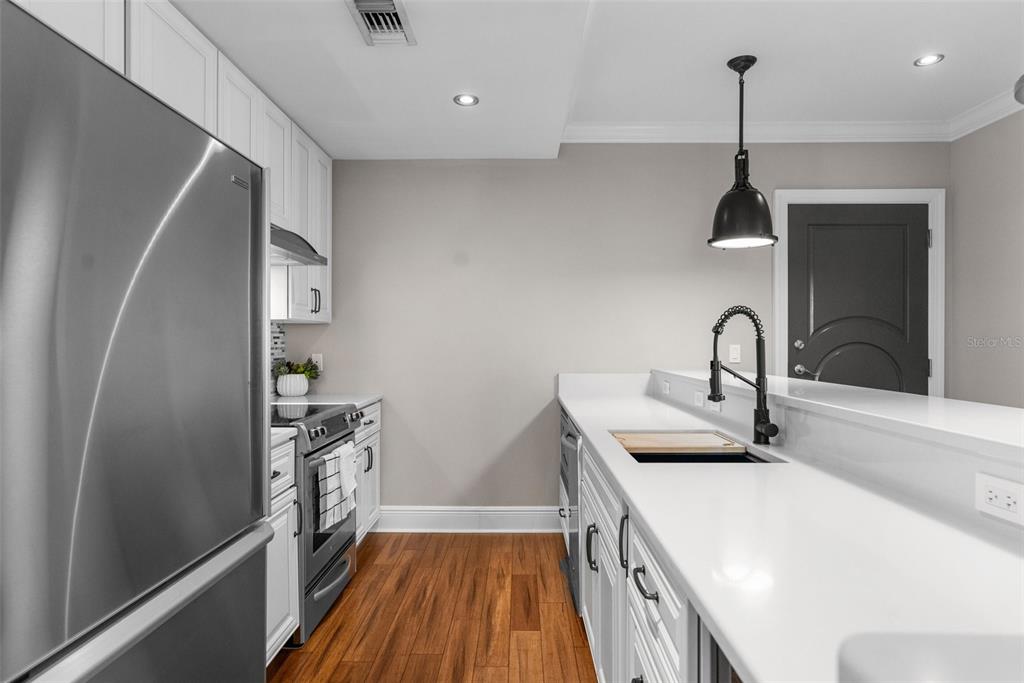 A kitchen features white cabinetry, stainless steel appliances, a white countertop, and wood flooring — 1238 E KENNEDY BOULEVARD UNIT 501, TAMPA, FL