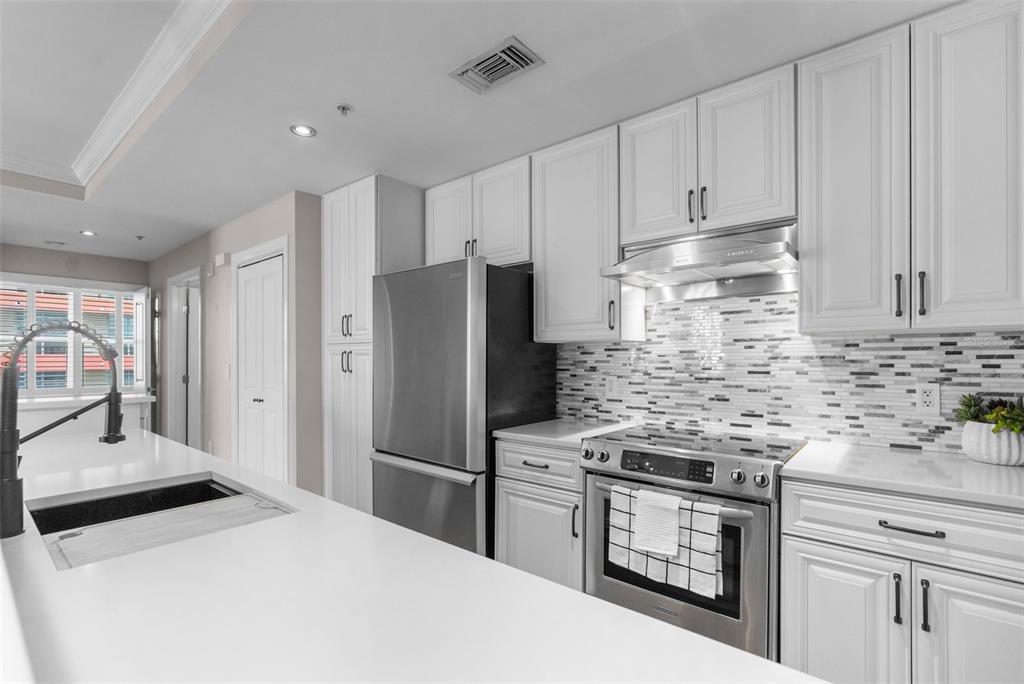 A modern kitchen features white cabinetry, stainless steel appliances, a quartz island, and a tiled backsplash — 1238 E KENNEDY BOULEVARD UNIT 501, TAMPA, FL