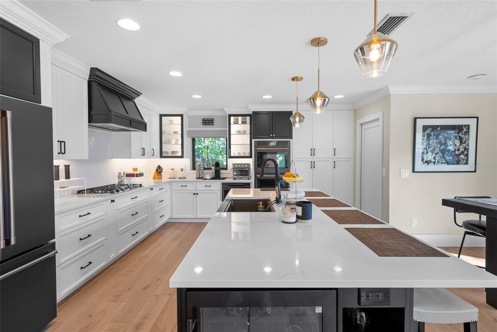 A modern kitchen features white cabinetry, a large quartz island, and black accents throughout — 4926 W MELROSE AVENUE N, TAMPA, FL