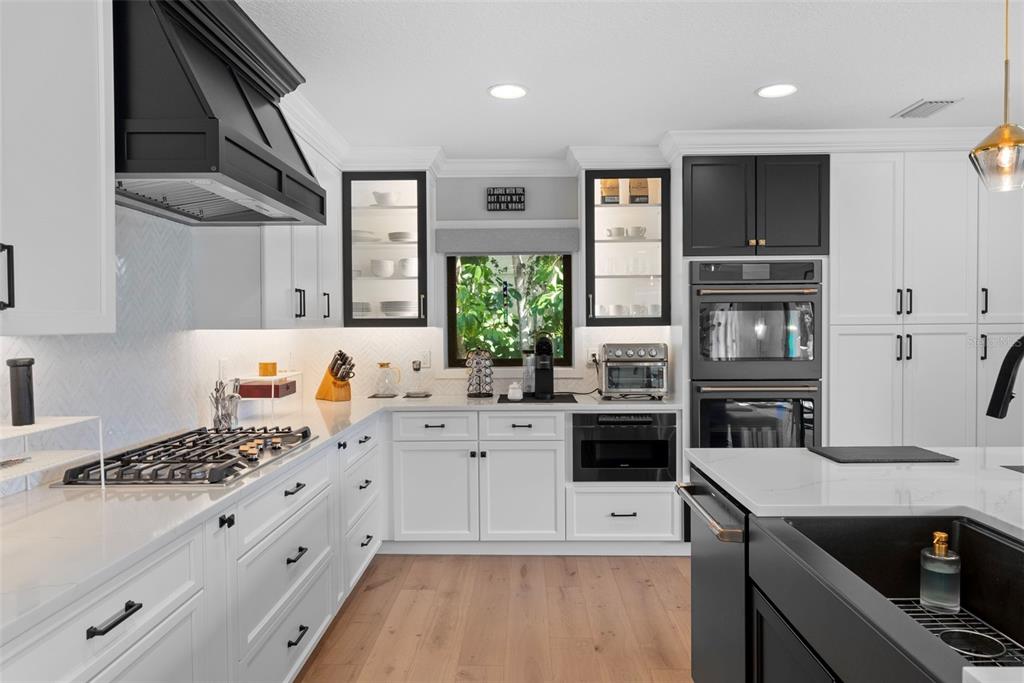 A modern kitchen features white cabinets, black accents, stainless steel appliances, and light wood flooring — 4926 W MELROSE AVENUE N, TAMPA, FL