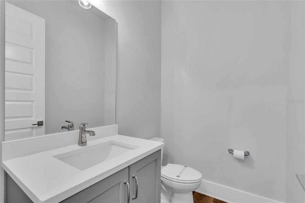 A modern half bathroom features a gray vanity, white countertop, large mirror, and toilet — 506 LAUREL PARK DRIVE UNIT 506, SARASOTA, FL