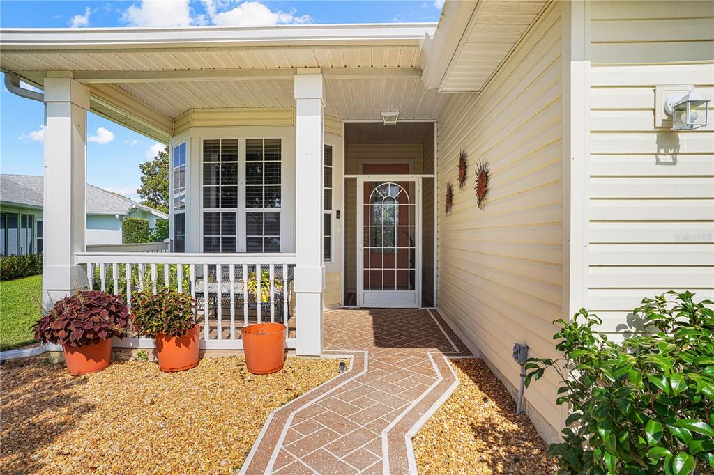 A covered front porch features a paved walkway, white railings, and potted plants — 4738 ST ANDREWS ARCADE, LEESBURG, FL