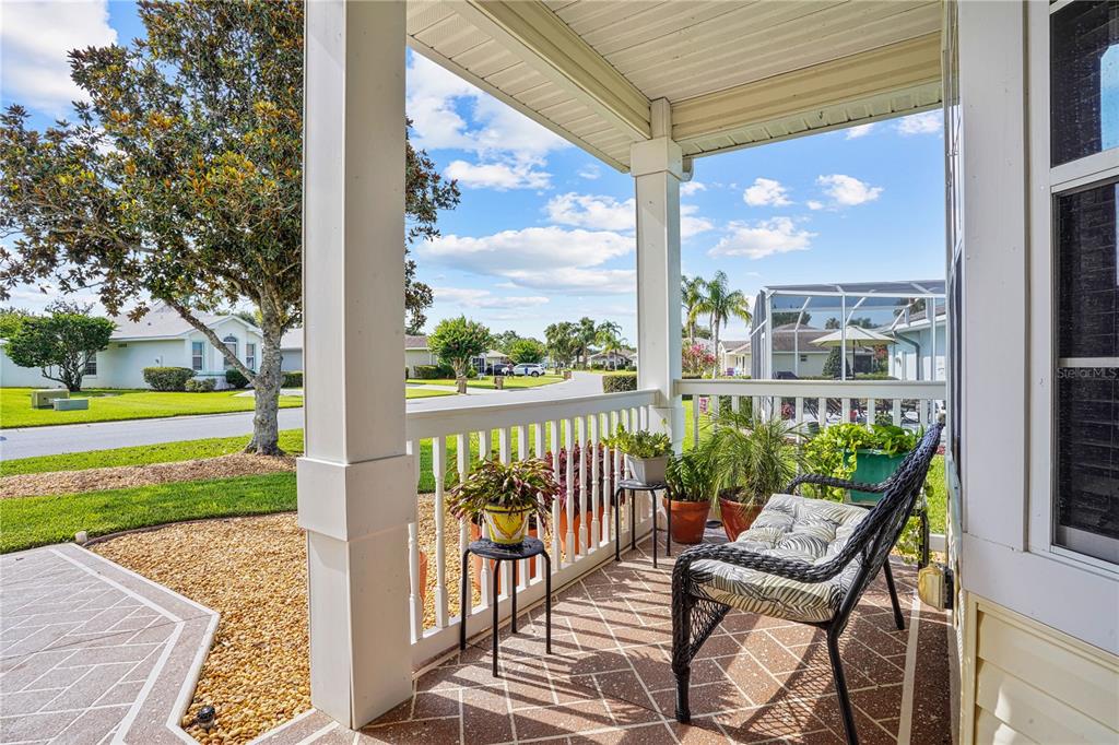 A covered porch features a patterned concrete floor, white railings, potted plants, and a bench — 4738 ST ANDREWS ARCADE, LEESBURG, FL