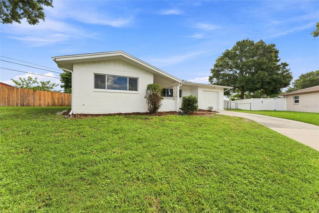 A white brick, single-story house features a front-facing garage, a concrete driveway, and a lawn — 1773 LONDON LN, CLEARWATER, FL