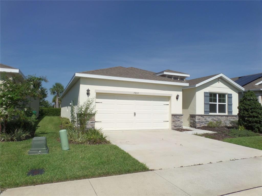 A single-story house with a beige exterior, stone accents, and a two-car garage — 7832 PENROSE PLACE, WILDWOOD, FL