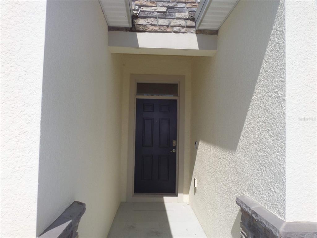 A dark front door is recessed within a stucco entryway featuring a stone accent wall — 7832 PENROSE PLACE, WILDWOOD, FL